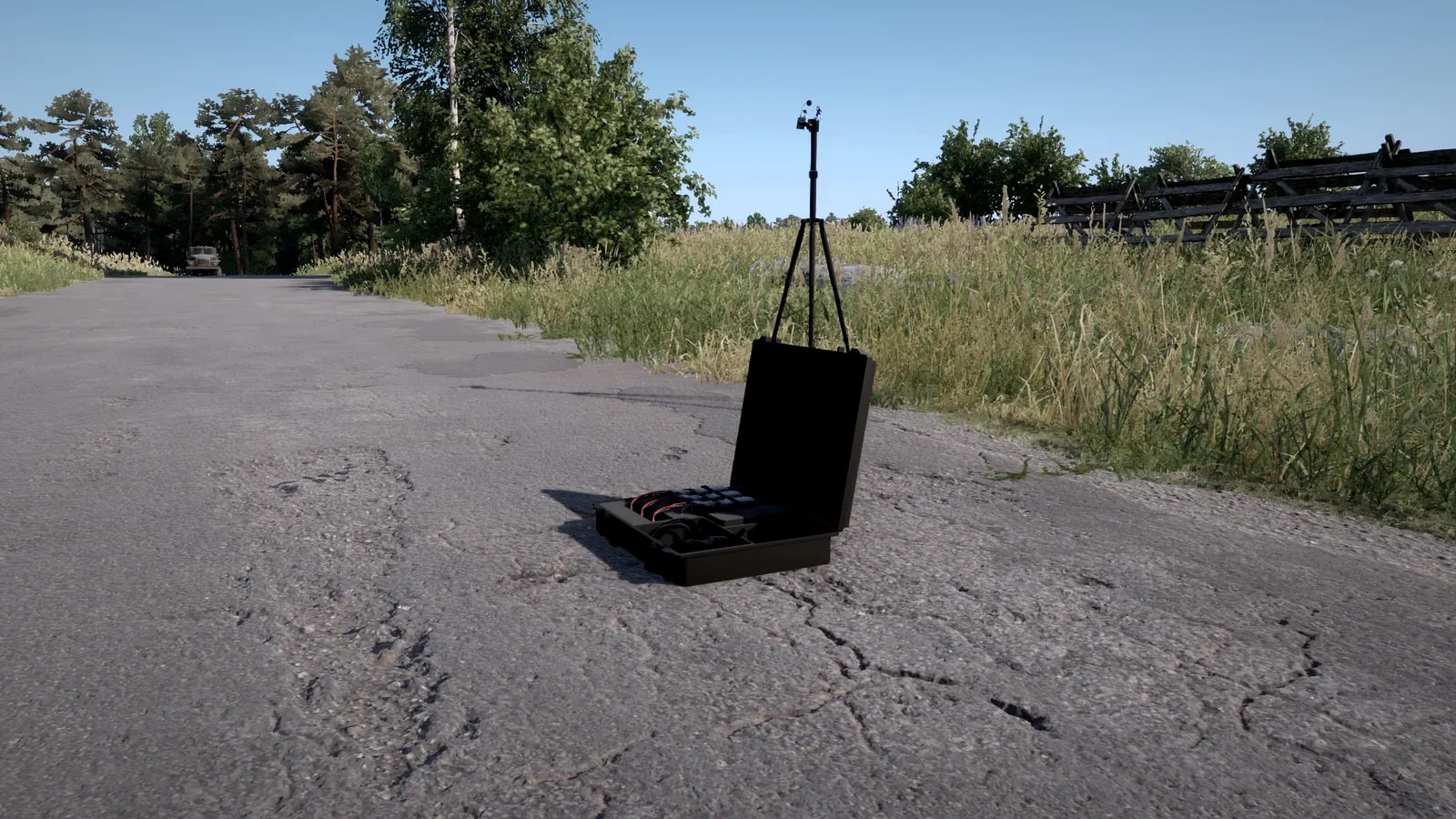 Estação de comando aberta no chão, com baterias e controles, e a antena do drone montada em um tripé logo atrás, à beira de uma estrada