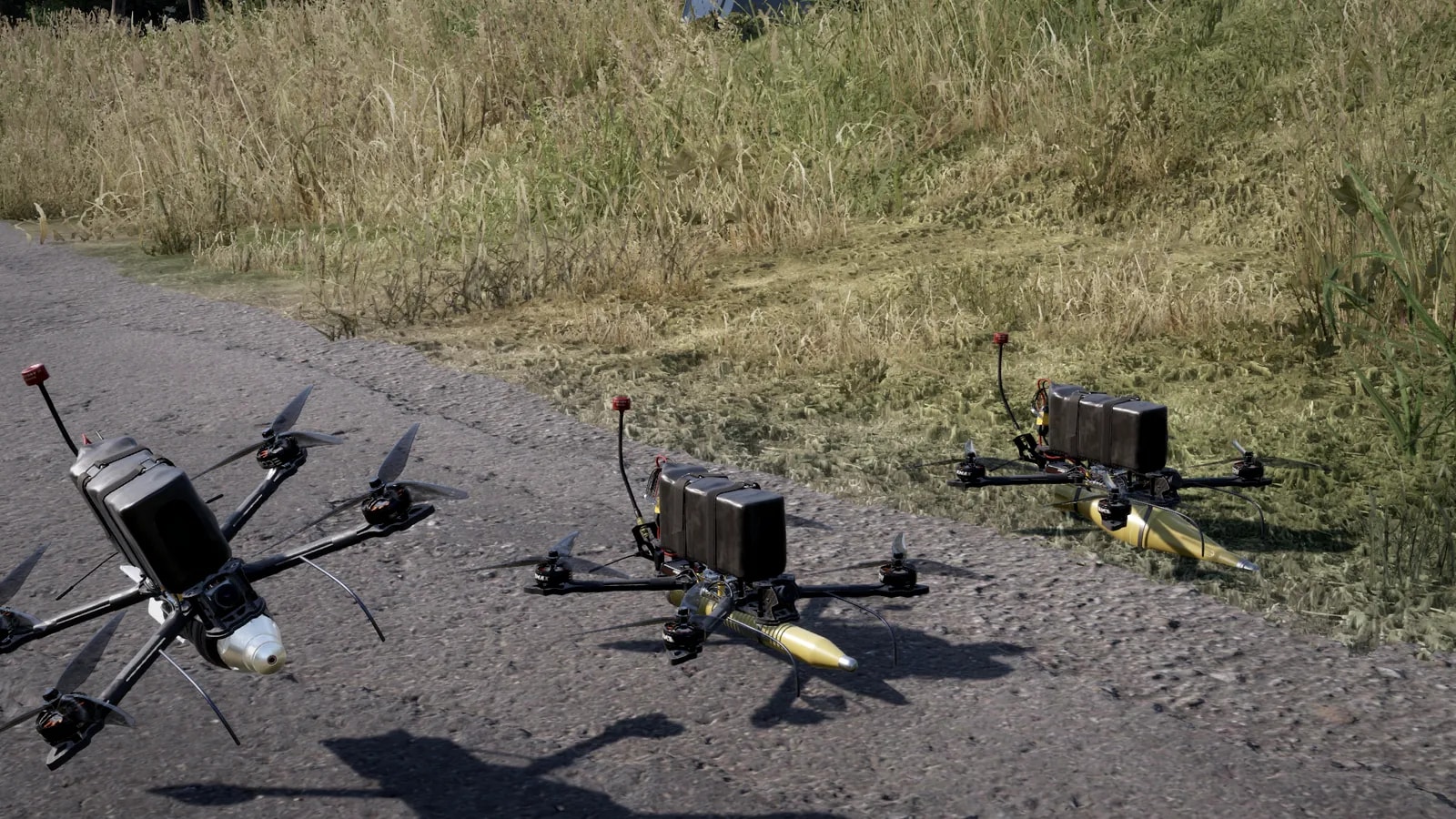 Três drones FPV kamikaze lado a lado na beira de uma estrada: na frente, um com ogiva branca e arredondada (OFCP); no meio, um com ogiva amarela e fina (OG7V); atrás, um com a ogiva amarela de RPG